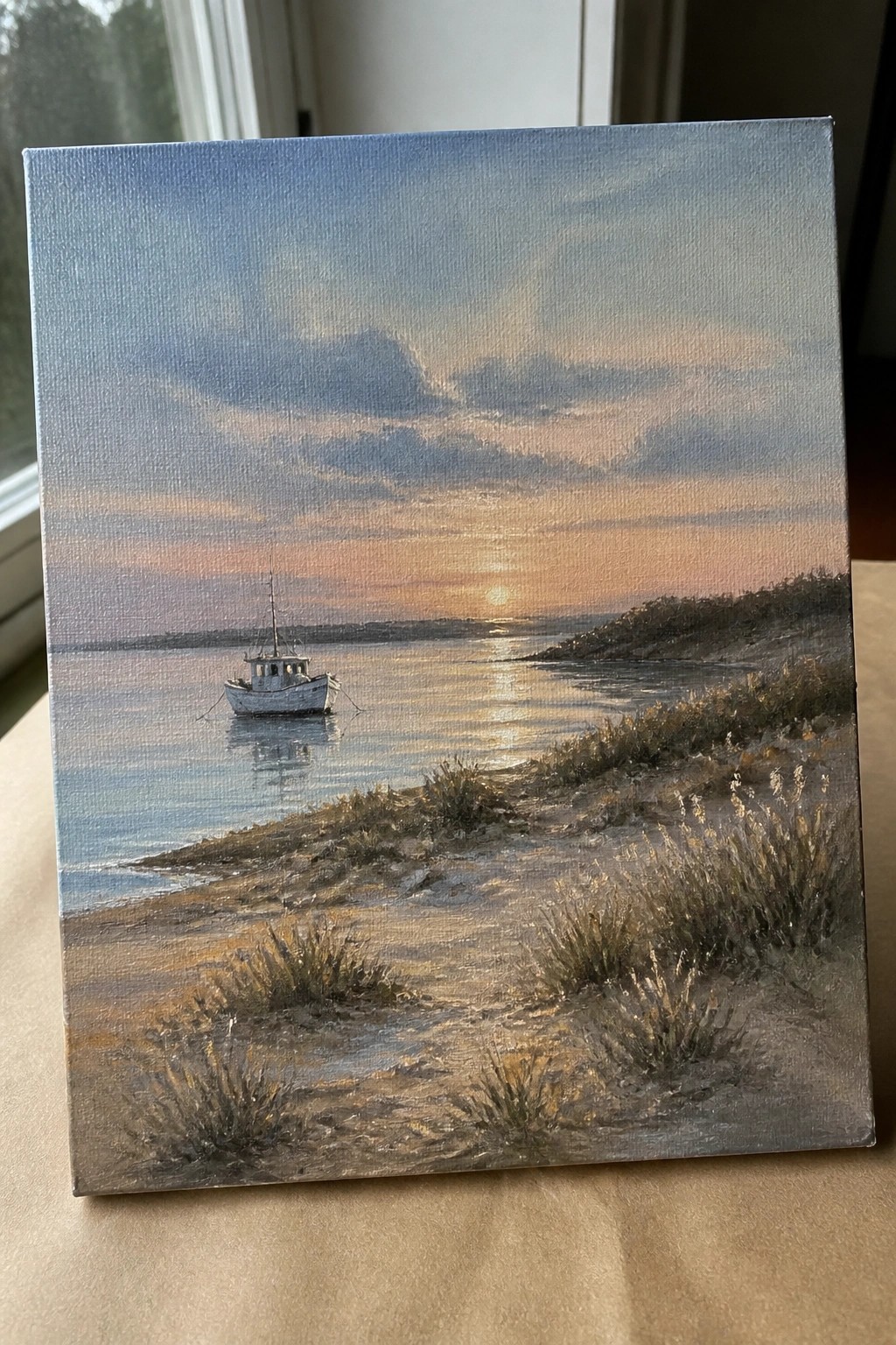 Lone white boat on calm waters at sunset near sandy grassy shore.