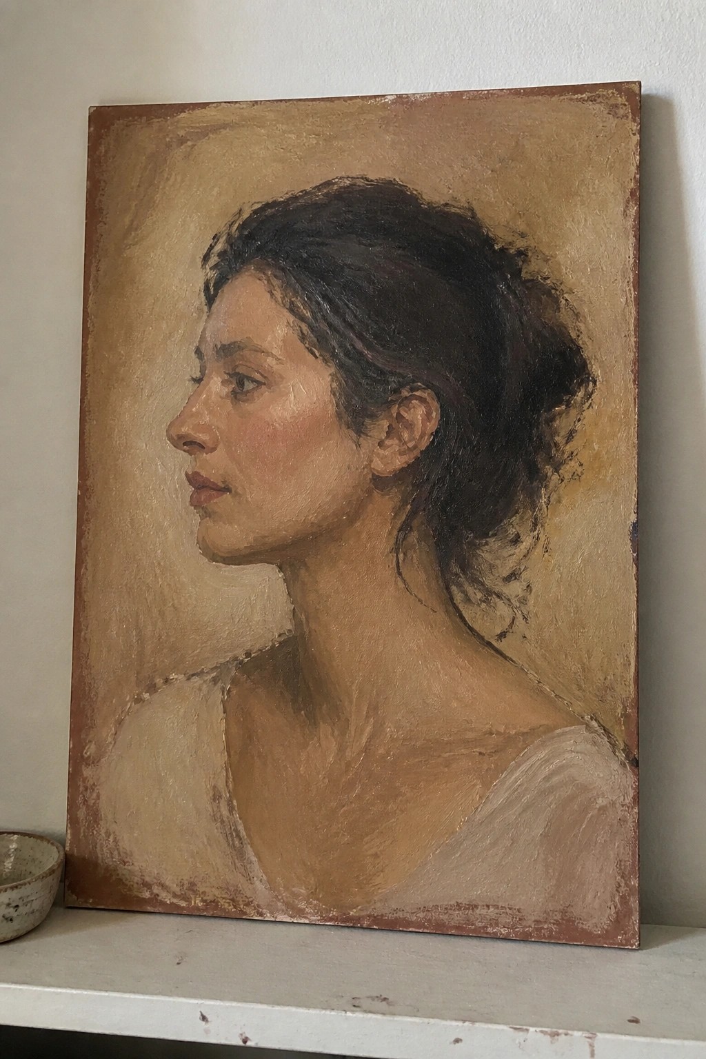 Woman in left profile with dark hair in bun, light top, on brown canvas beside small bowl.