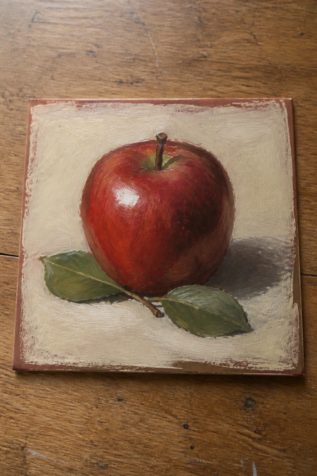 Realistic still life painting of glossy red apple with green leaves on canvas