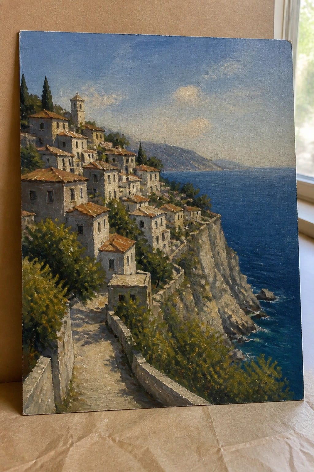 Realistic oil painting of a white stone village on a cliff above the sea with a path running down through the buildings.