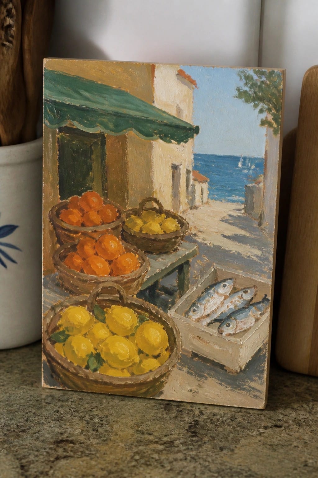 An oil painting of baskets of oranges and lemons beside a crate of fish on a sunny street with sea and buildings in the background.