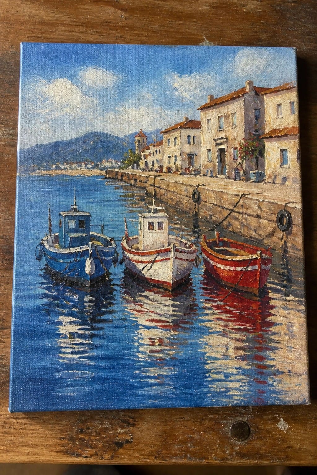 Colorful boats docked by stone wall with reflections in blue water and hillside village.