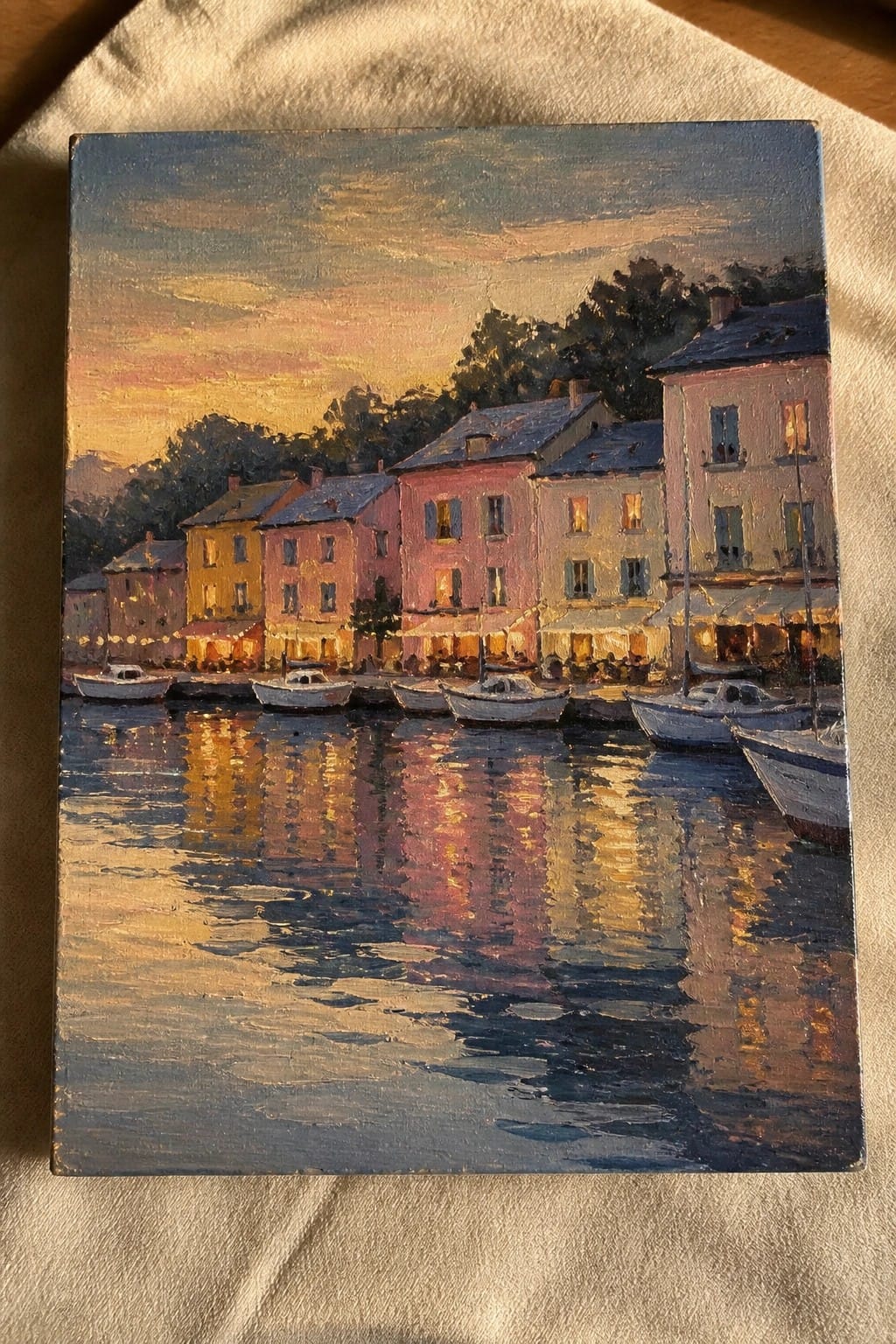 Oil painting of colorful houses by a harbor with boats reflecting sunset hues on water