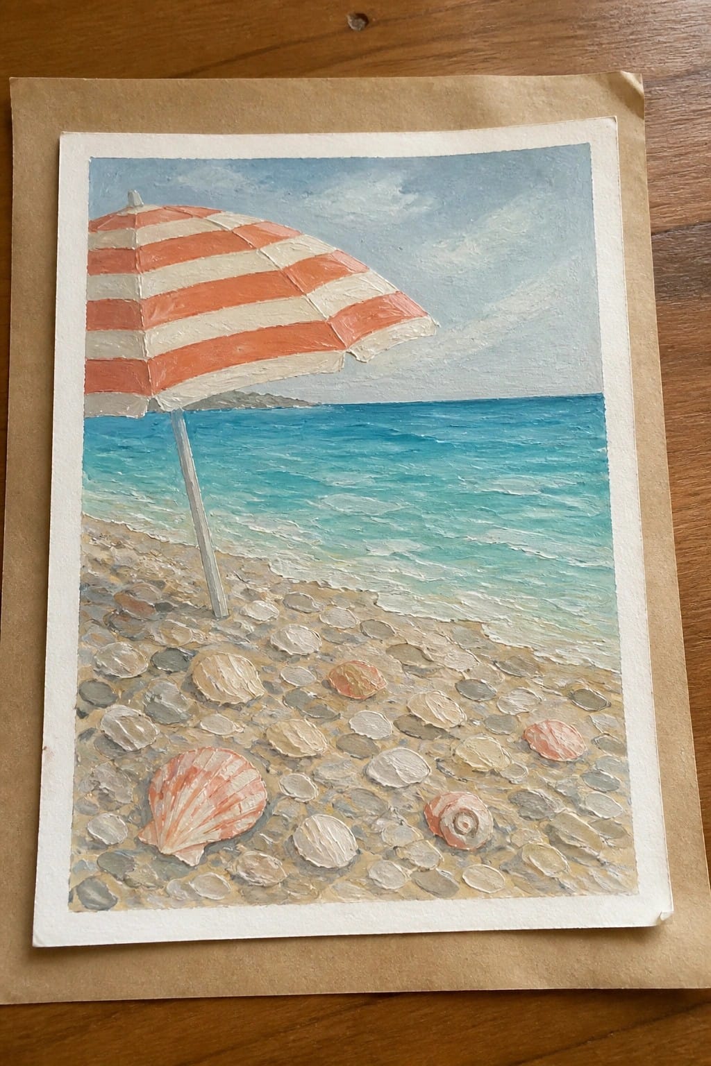 Red and white striped umbrella on pebble beach with seashells and blue sea.