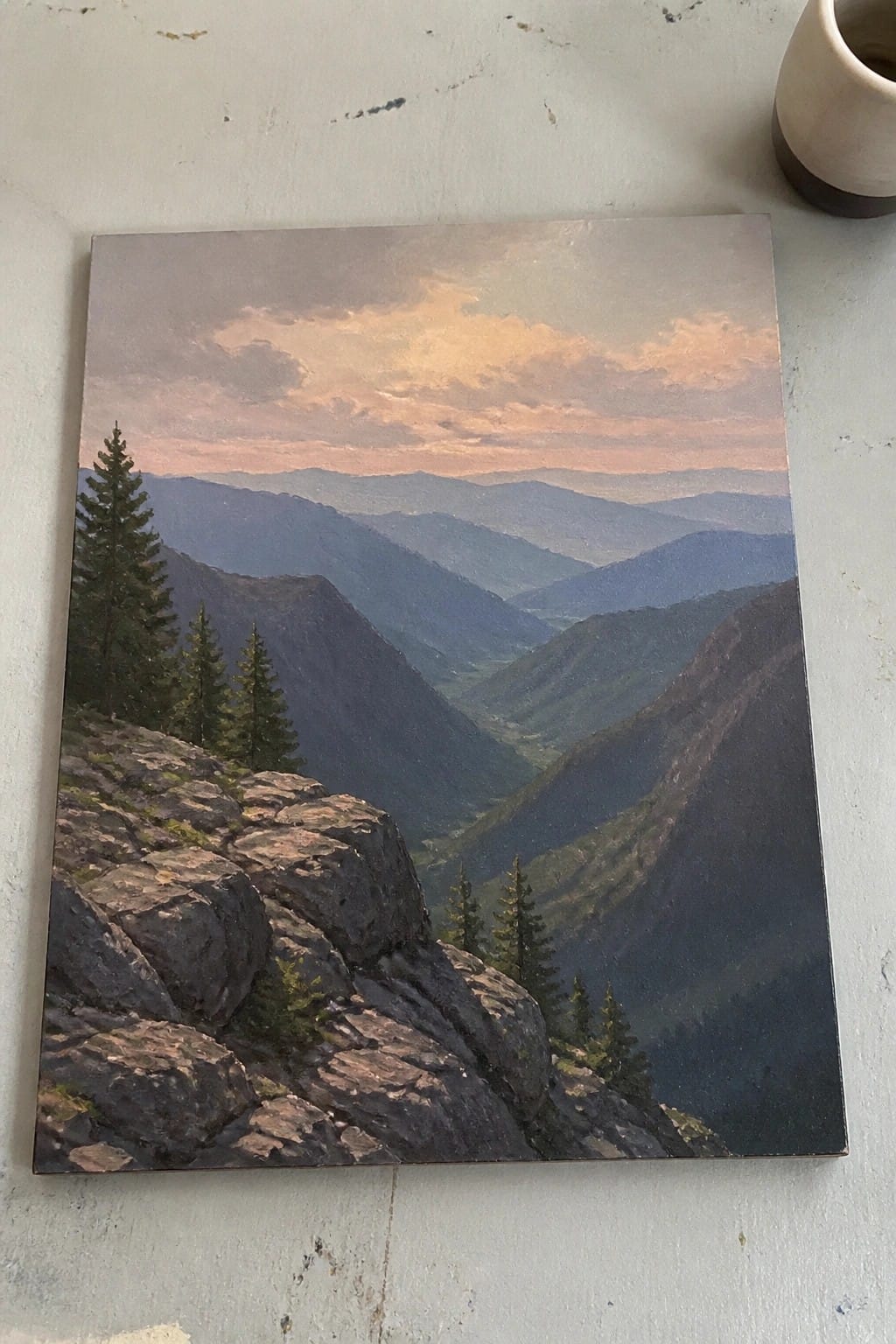 Mountain landscape painting with pine trees on rocks overlooking hazy valleys under pink sky.