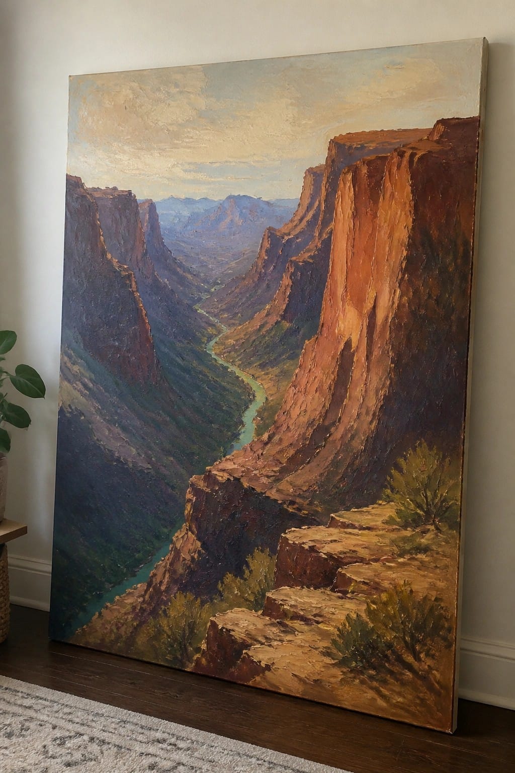 Large oil painting of red canyon cliffs and winding river leaning indoors.