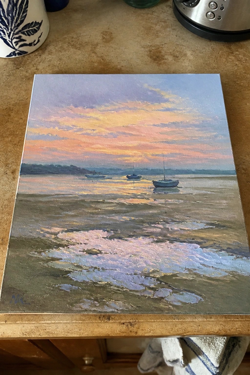 Seascape painting of boats on tidal flats under pink-orange sunset sky on countertop
