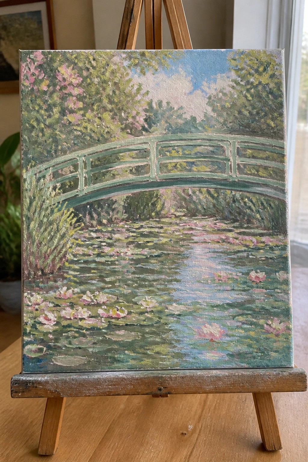 Impressionist painting of green bridge over pink water lilies on wooden easel