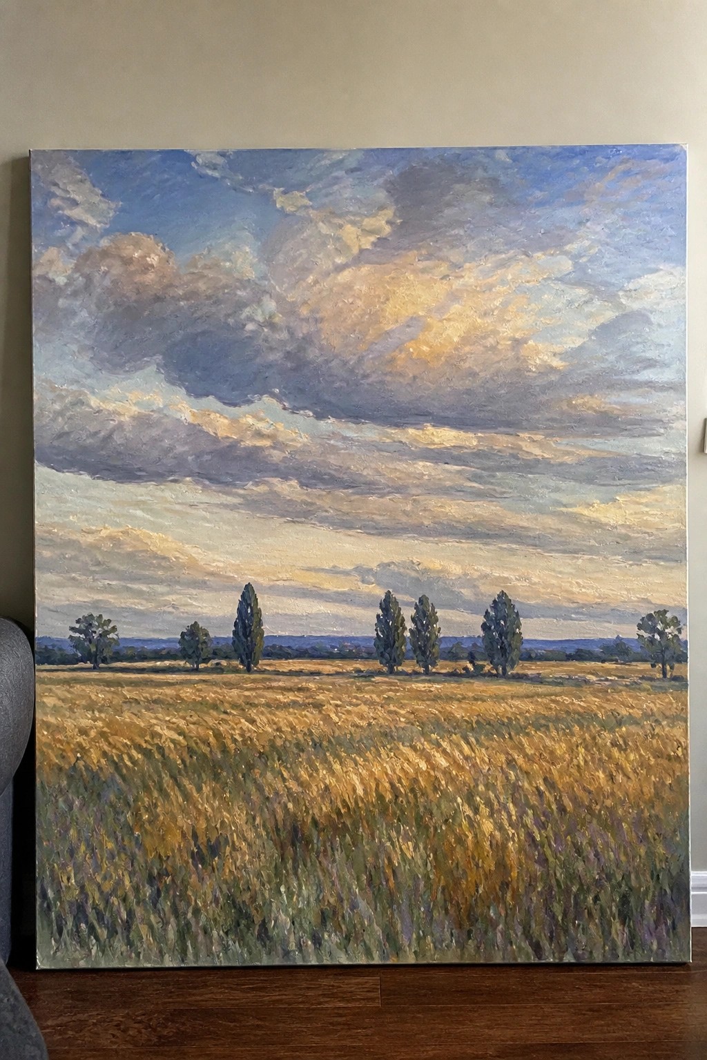 Golden wheat field under dramatic blue and gold clouds with scattered trees at dusk