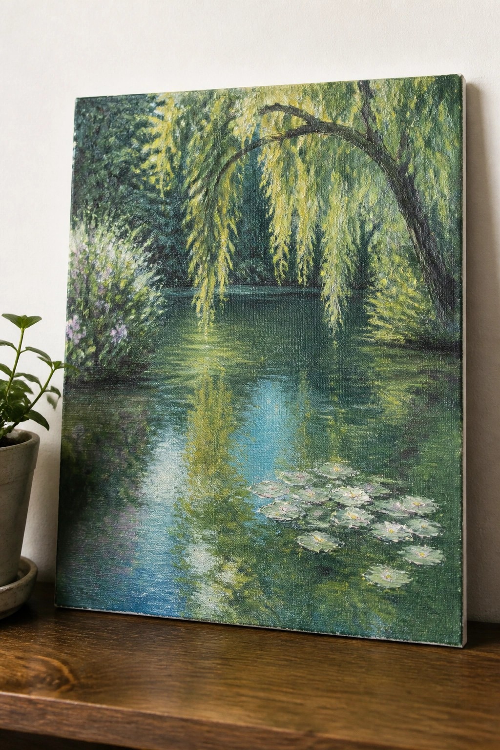 Painting of a green pond with weeping willow and lily pads beside a potted plant.