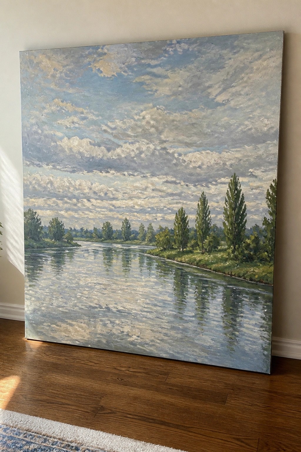 Large impressionist painting of reflective river, trees, and cloudy sky on wooden floor