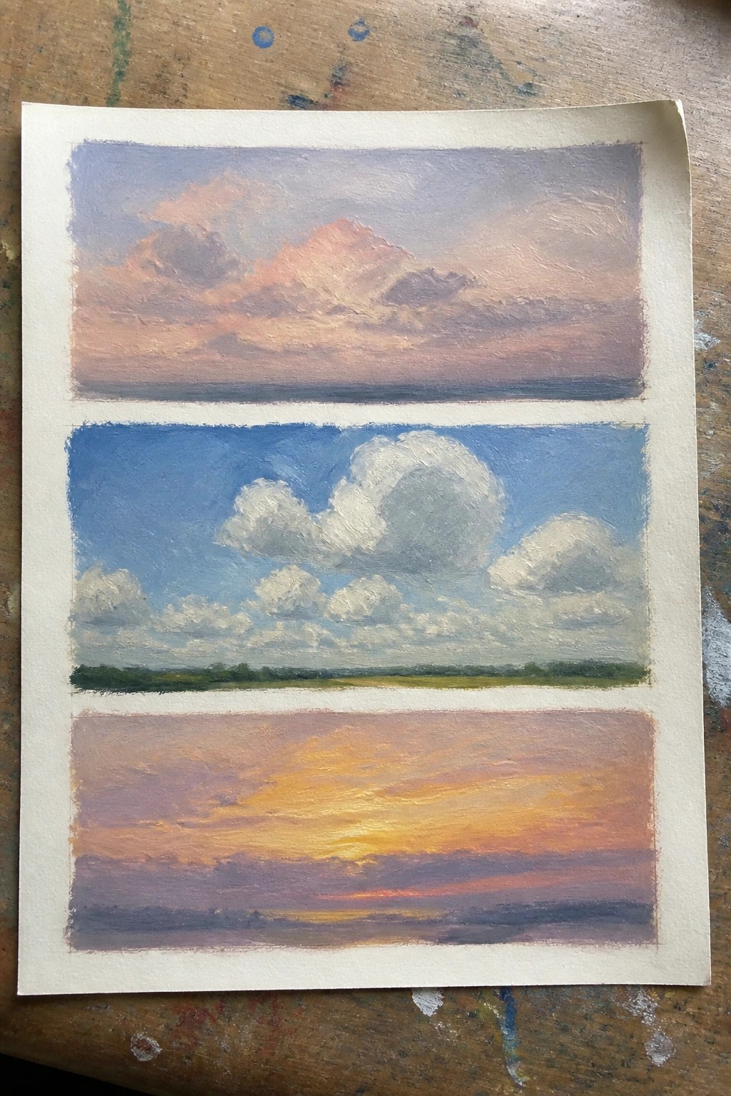 Three stacked sky paintings in pink, blue, and orange hues on paper.